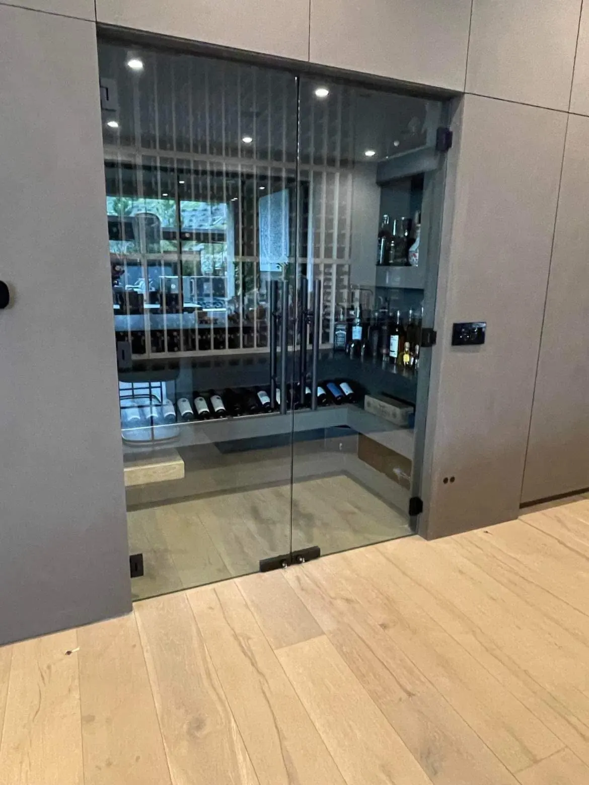 Frameless glass wine-cellar doors set flush into a paneled wall