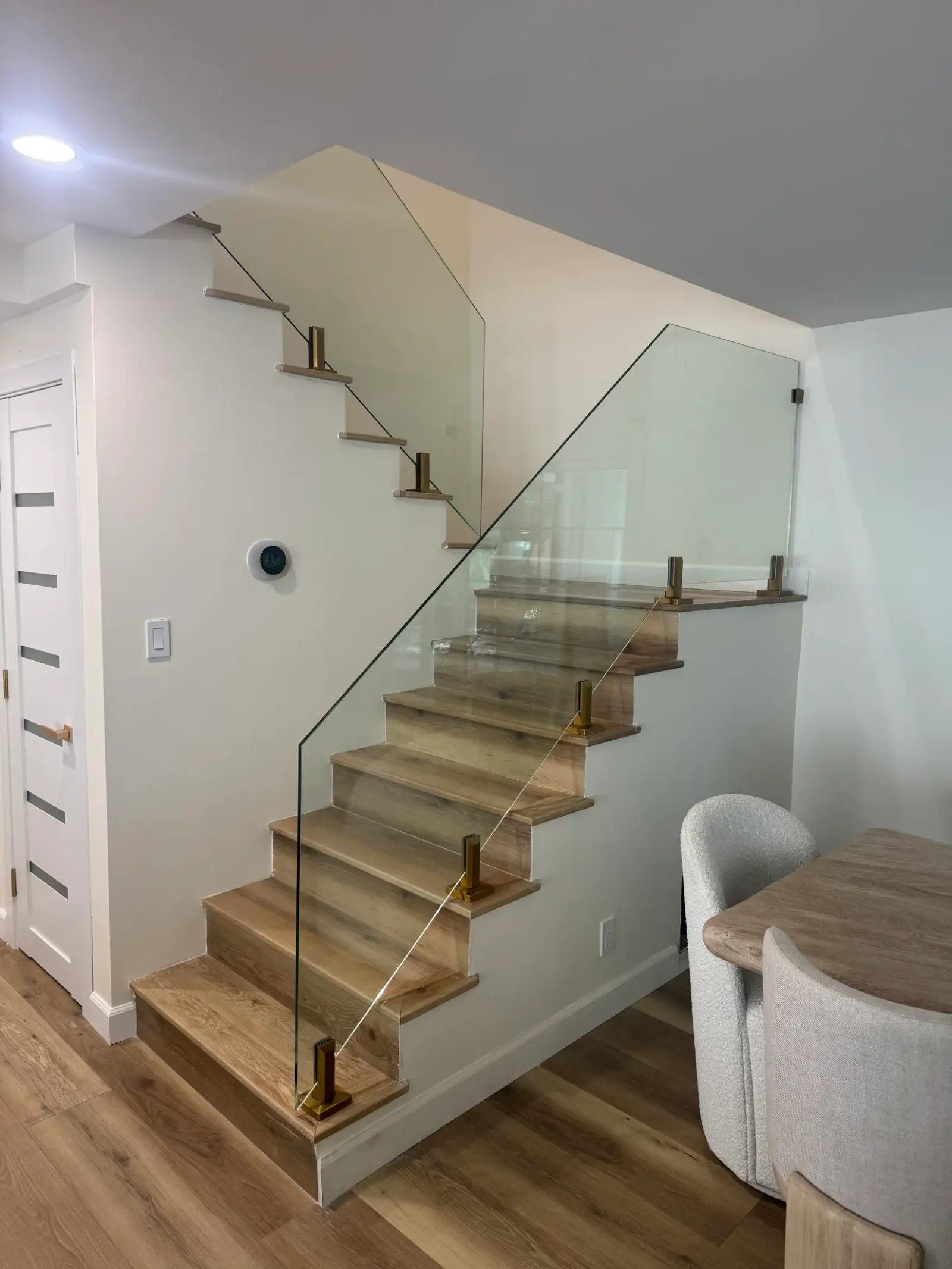 Frameless glass stair railing mounted with brass standoffs on light oak stairs