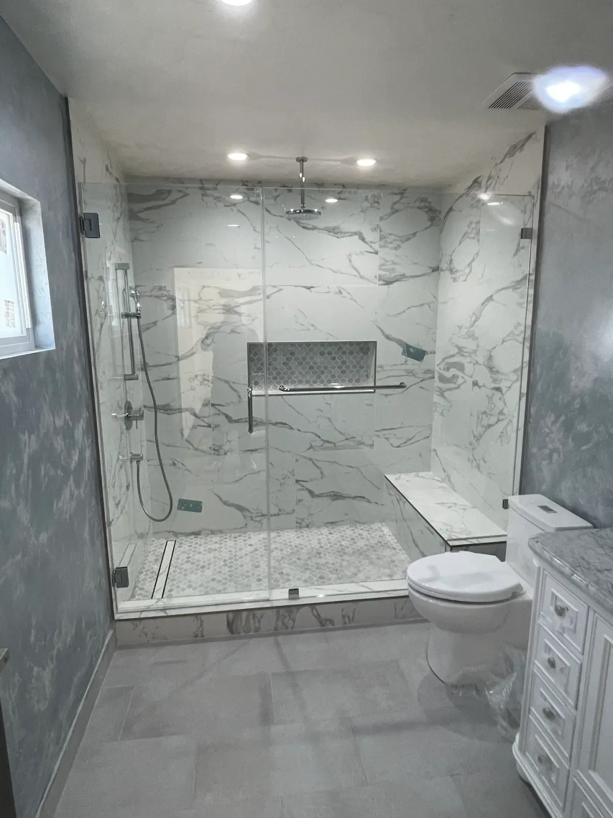 Frameless panel-and-door shower with chrome hardware and a marble bench