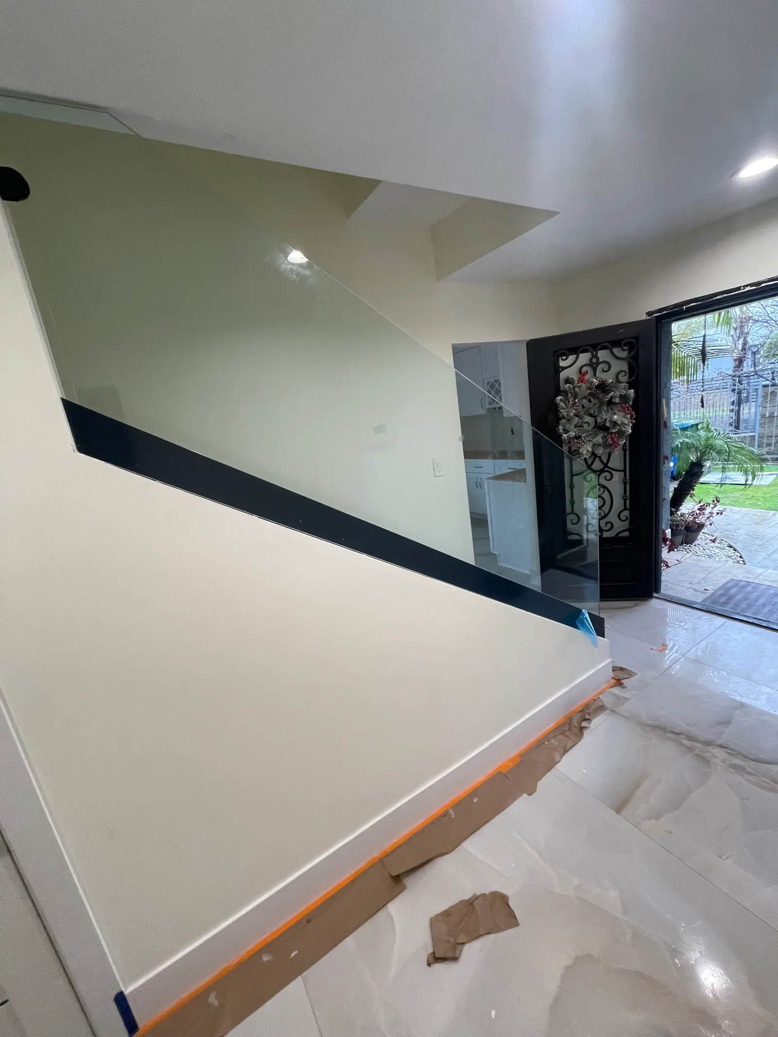 Glass landing railing with a black cap rail overlooking a tiled entry hall