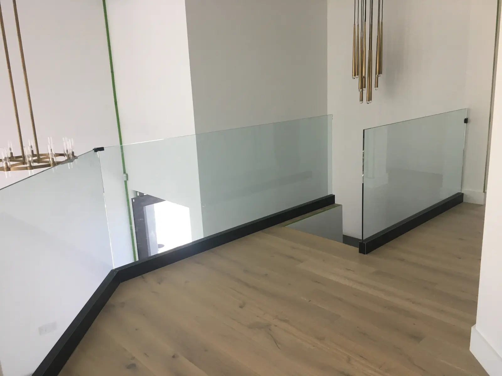 Glass landing railing set in a black base shoe on a wide-plank oak floor