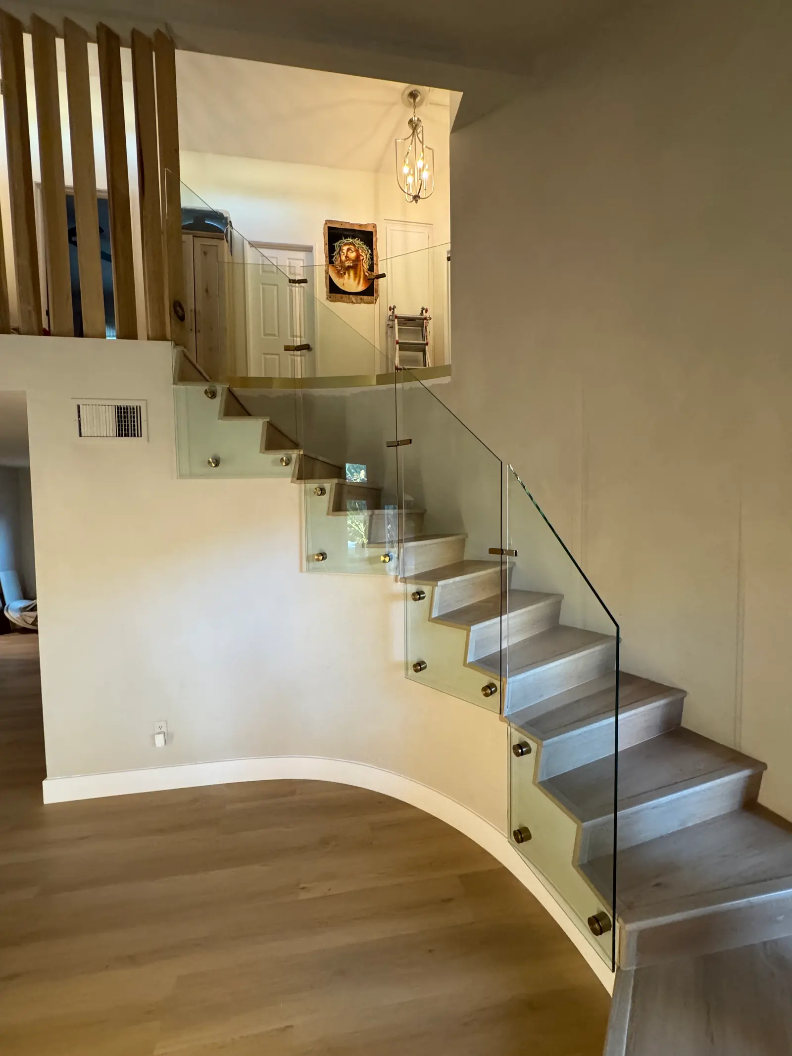 Curved glass stair railing on brass standoffs following a winding staircase