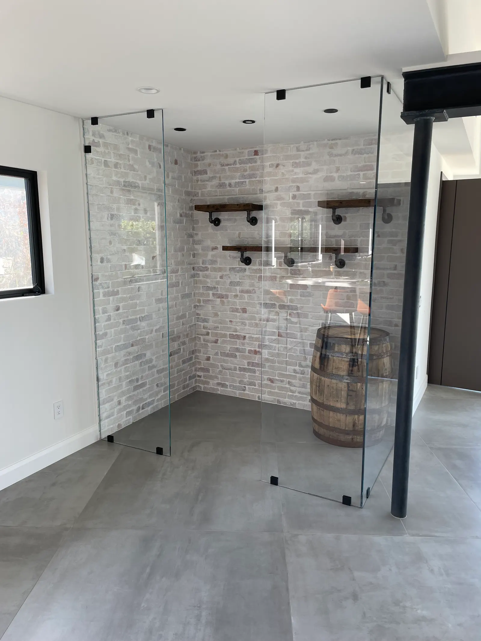 Frameless glass partition panels with matte-black clamps enclosing a brick-walled tasting room