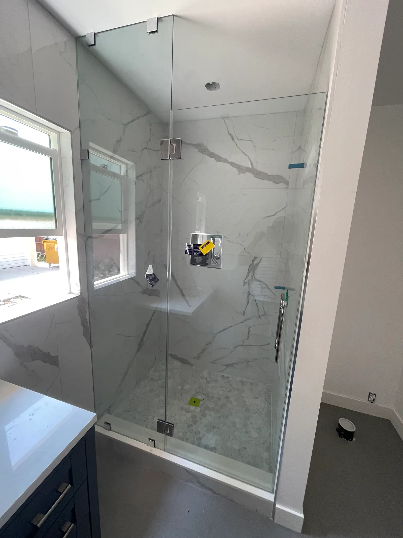Frameless shower door and inline panel with polished-chrome hinges against calacatta-look porcelain