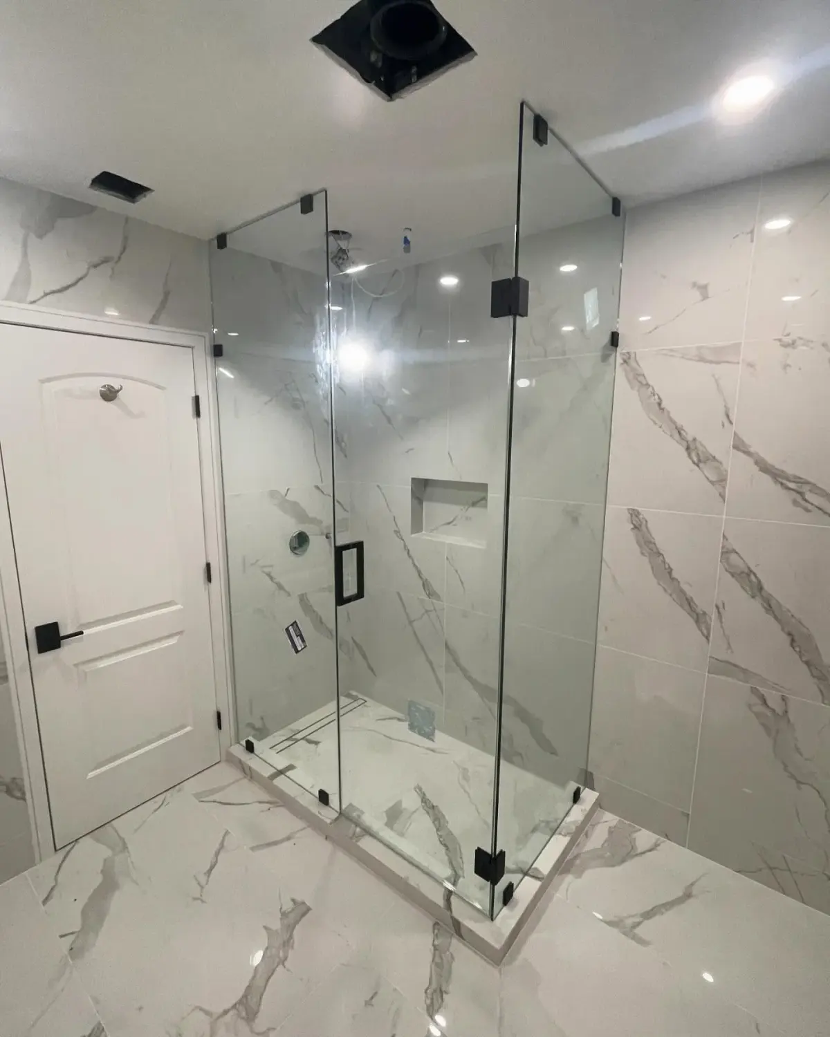 Frameless corner shower enclosure with matte-black hinges and clips in a white marble bathroom