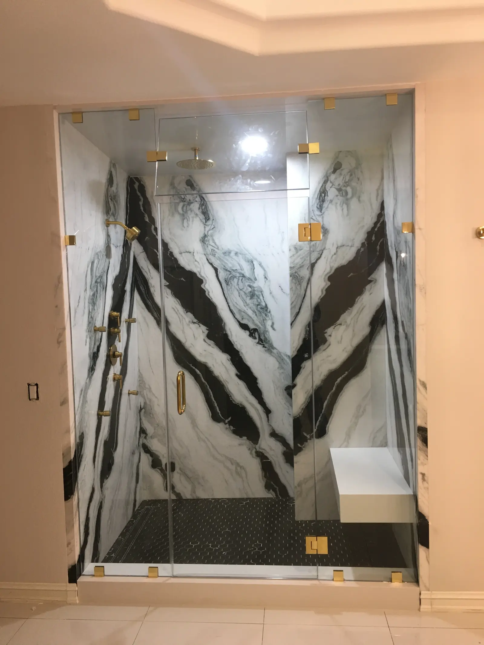 Frameless shower enclosure with brushed-brass clips and a floating bench in bookmatched panda marble
