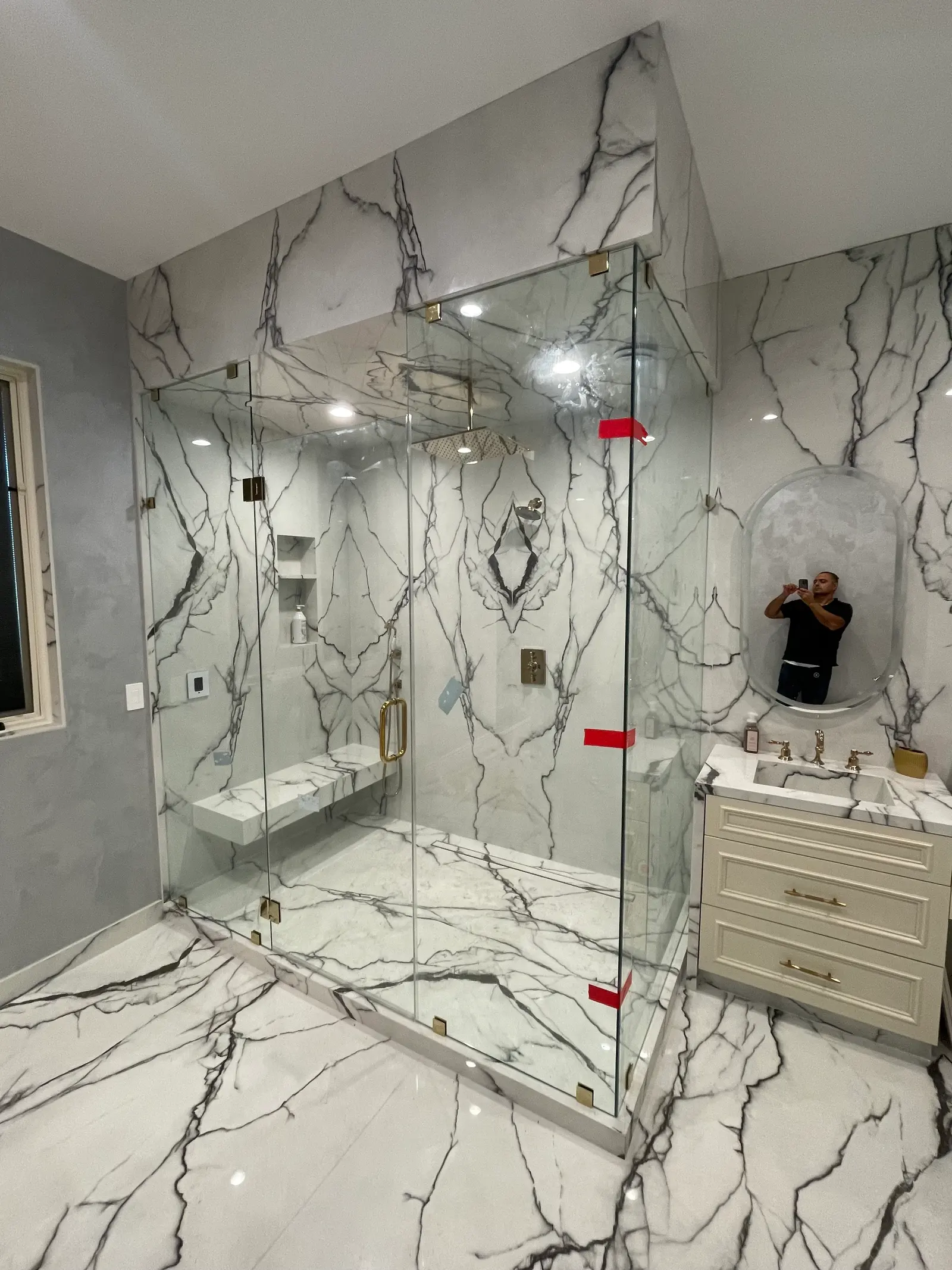 Large frameless enclosure with brass clips and a stone bench in dramatically veined white marble