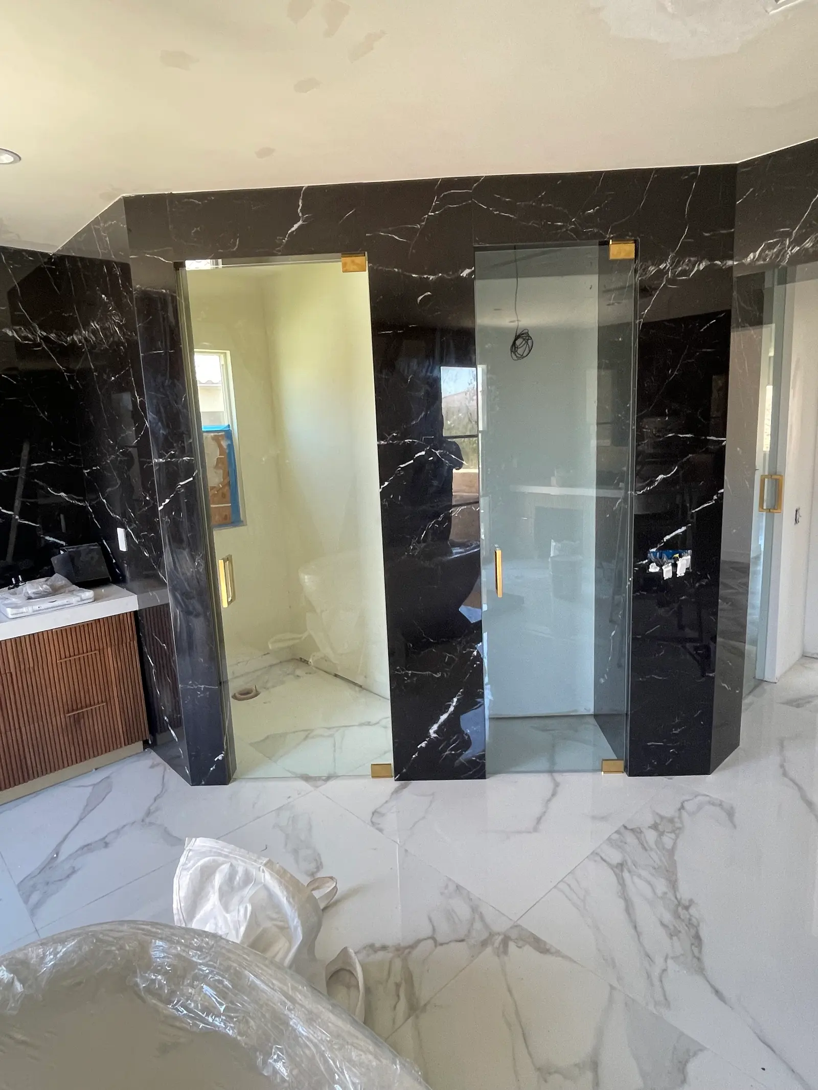Two frameless glass doors set into a black marble steam room with brushed-brass hardware