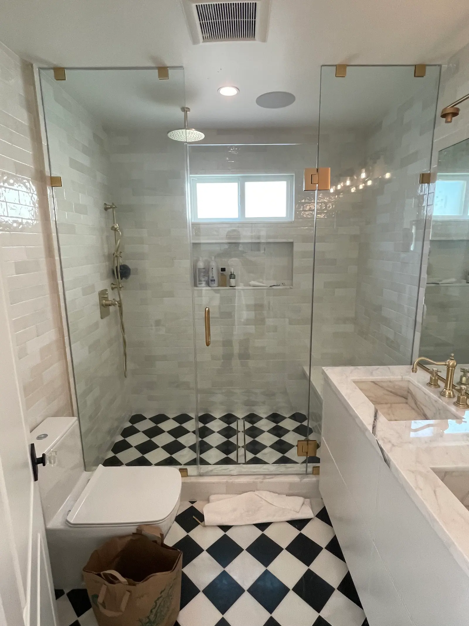 Frameless corner shower with brushed-brass hardware over a black-and-white checkerboard floor