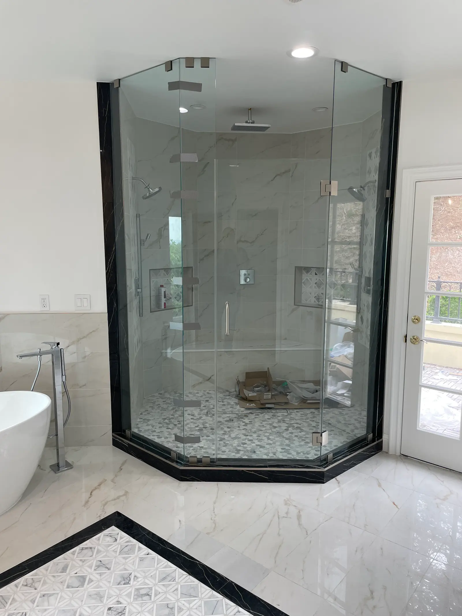 Full-height neo-angle shower enclosure on a black marble curb, with a mosaic pan and marble walls