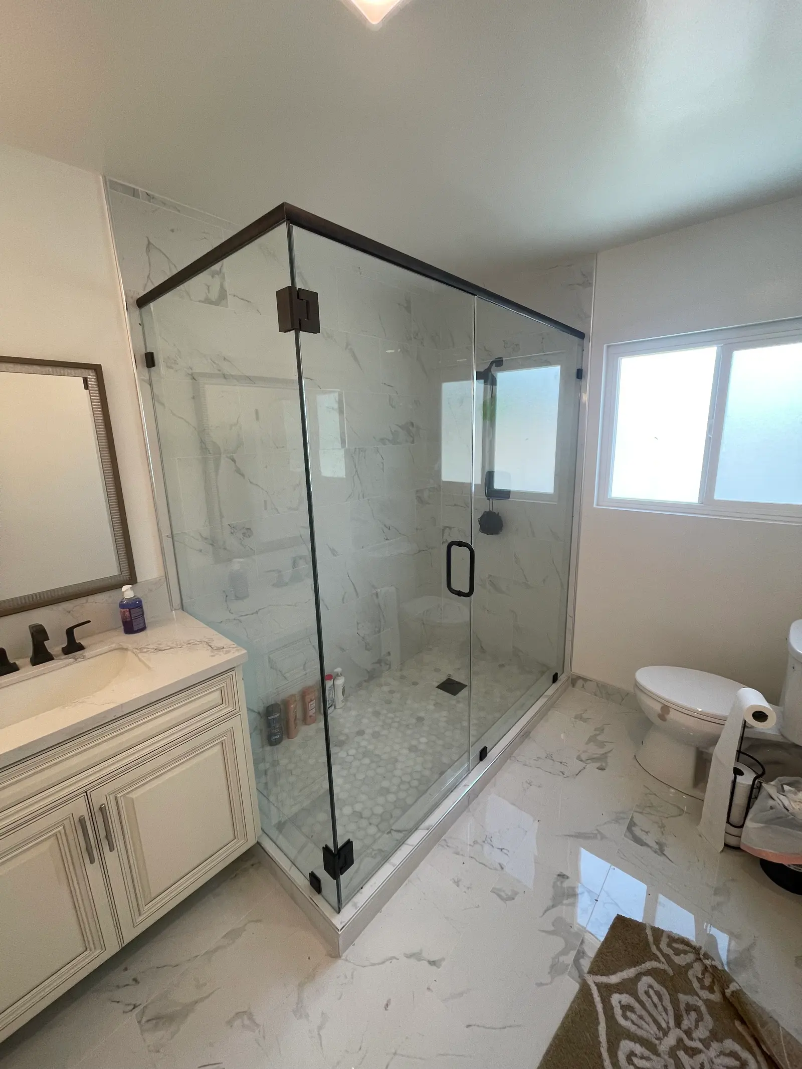 Frameless corner shower with oil-rubbed bronze clips and a marble mosaic pan