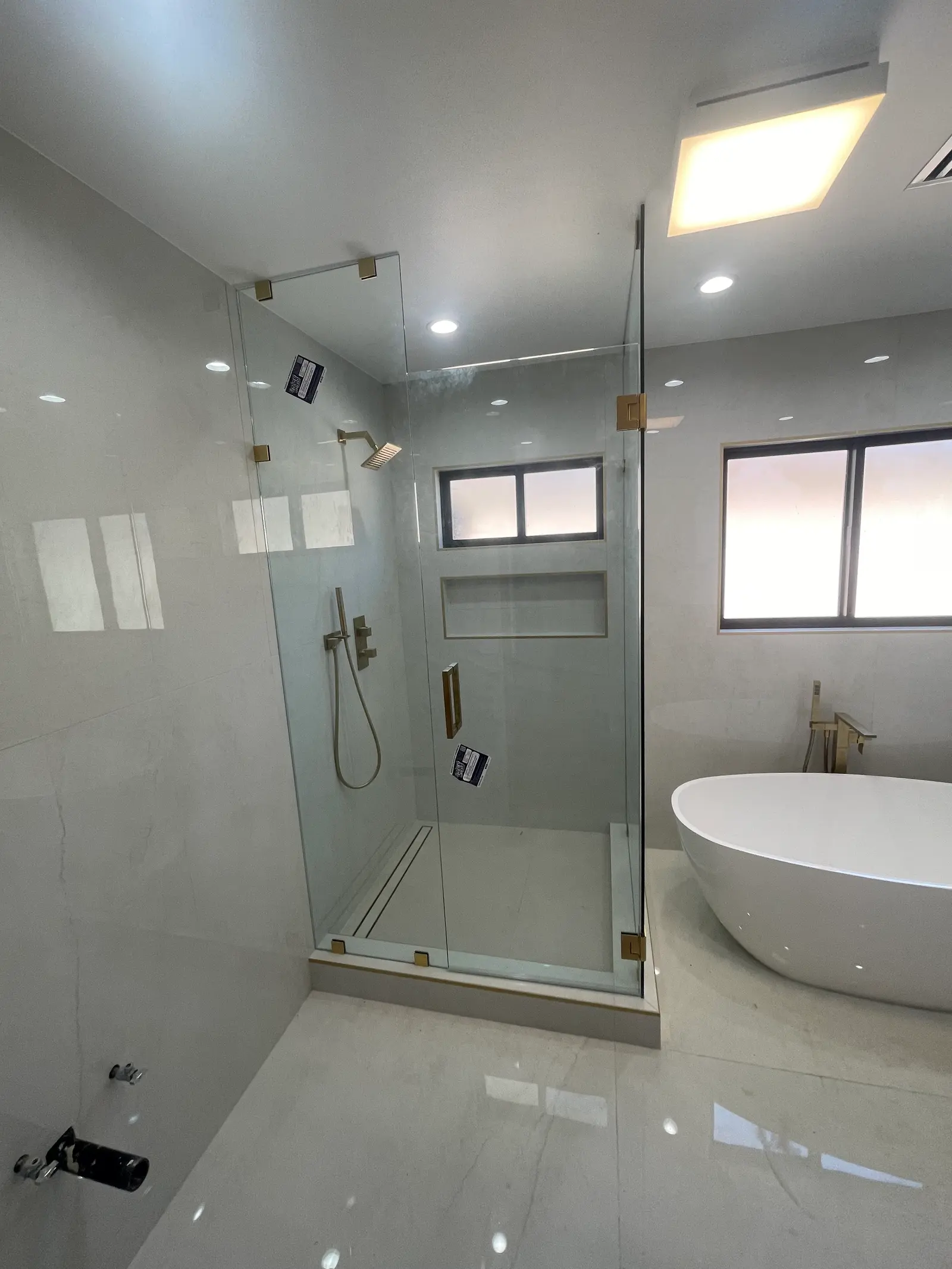 Frameless corner shower with brushed-brass hardware next to a freestanding soaking tub
