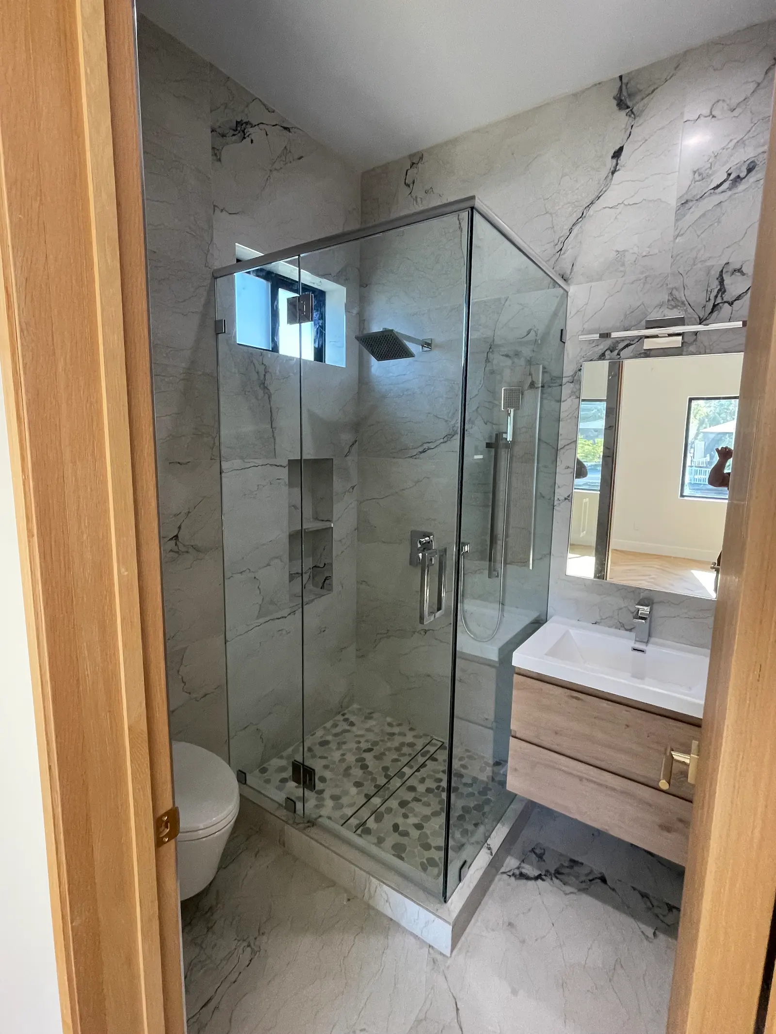 Neo-angle frameless shower enclosure with chrome hardware and a pebble-mosaic floor