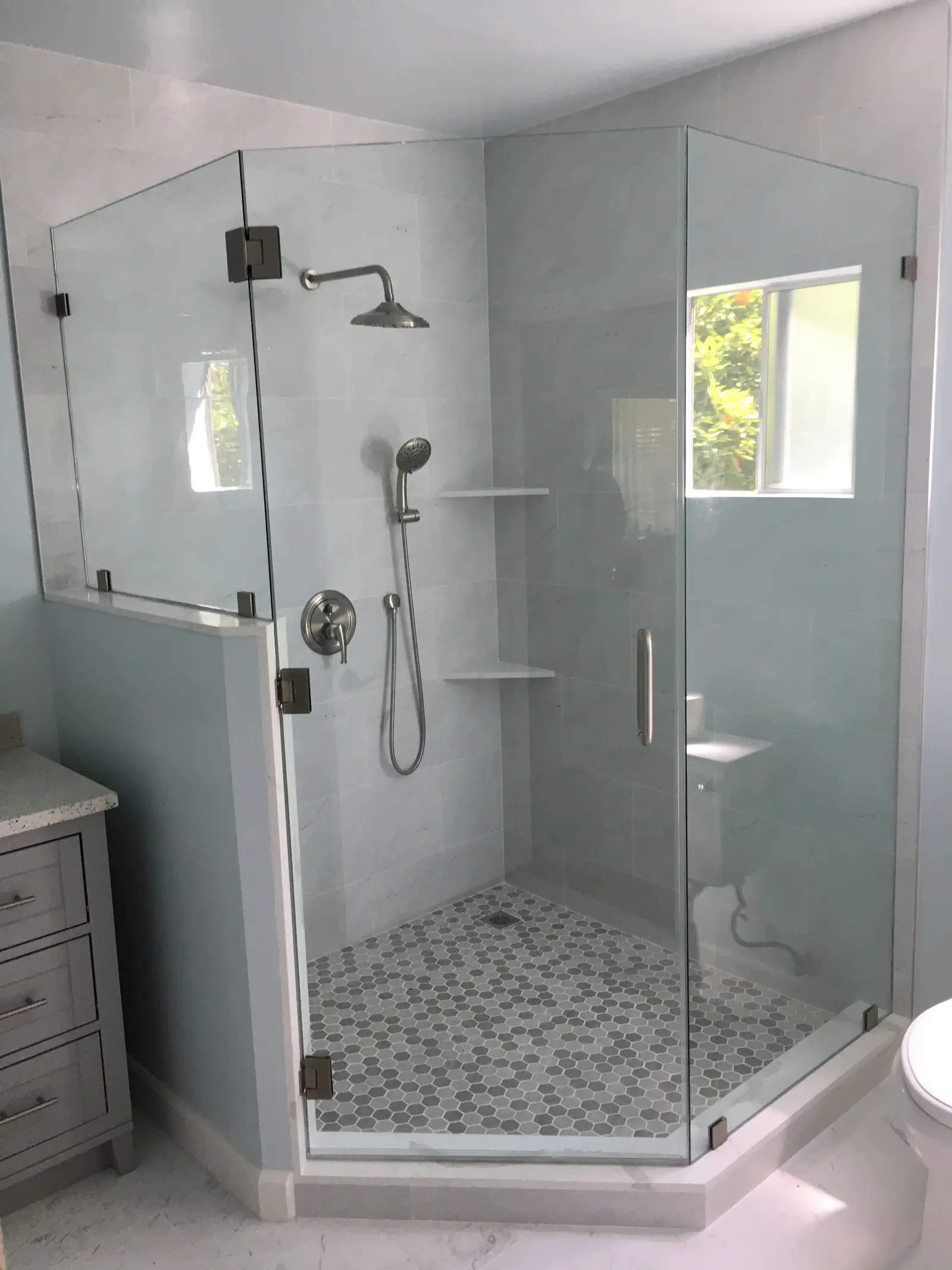 Neo-angle frameless shower enclosure with oil-rubbed bronze hinges and a marble hex-tile floor