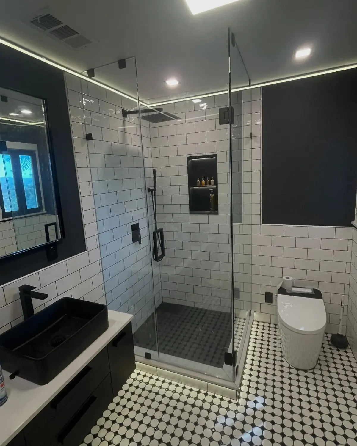 Frameless corner shower with matte-black hardware in a black-and-white subway-tile bathroom