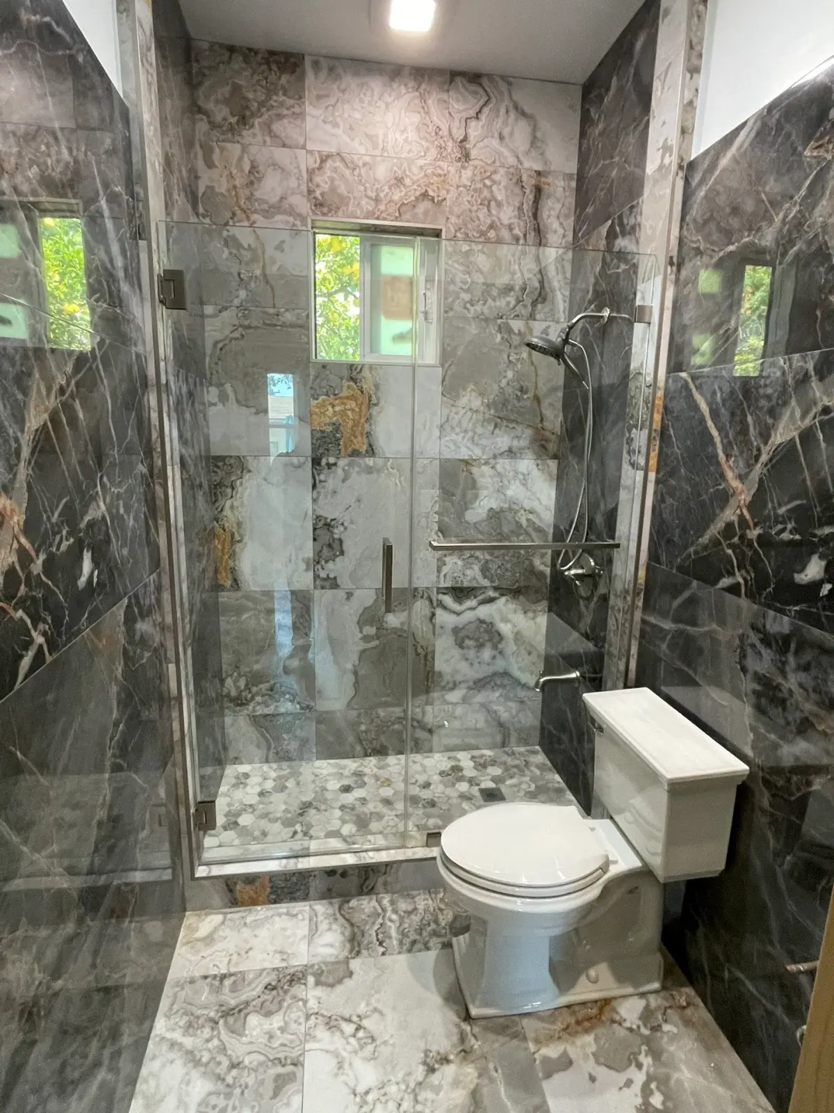 Frameless shower door with a brushed-nickel handle set in dramatic gray onyx-look stone
