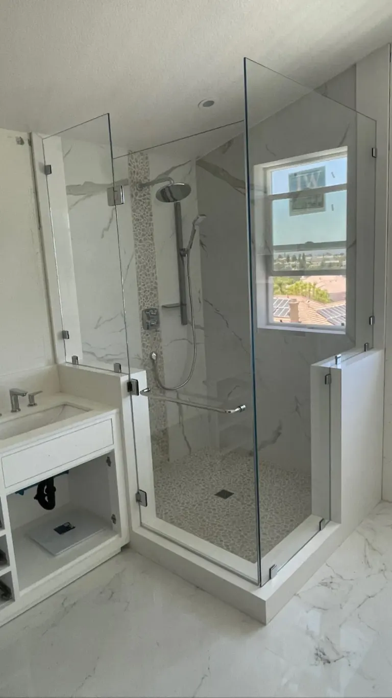 Frameless corner shower glass mounted over a half wall, with chrome hardware and a pebble-tile pan