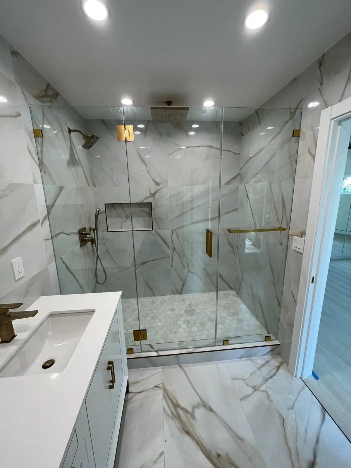 Frameless shower enclosure with brushed-brass hinges and handle in a calacatta-gold marble bathroom